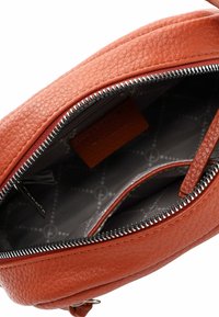 Borsa rotonda in pelle arancione con superficie texture. L'apertura completamente zip presenta un interno grigio con un motivo e una piccola tasca.