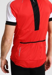 Jersey de ciclismo rojo con mangas cortas blancas, que cuenta con una raya vertical negra y detalles reflectantes. Cintura elástica con bolsillos de almacenamiento en la parte trasera.