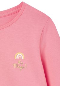 Pink fabric with a small pastel rainbow above the yellow text "it's Magic!" on the chest area of a shirt.