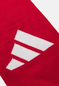Țesătură roșie tricotată cu un logo alb triunghiular proeminent. Textura este netedă, cu o culoare uniformă și margini curate.