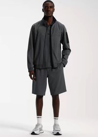 Mans sportklädsel med en mörkgrå zip-up jacka och matchande shorts, tillverkade av lätt material, med vit logotyp och sneakers.