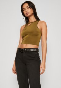 Olívazöld crop top, kulcslyuk alakú kivágással, magas derekú fekete nadrággal és textúrált fekete övvel, fém díszítésekkel.