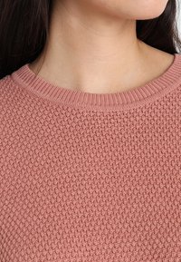 Texturerad, rosaröd tröja med en stickad mönster och rund halsringning. Tyget verkar mjukt med ett ribbat krage.