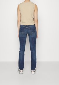 Beige ärmlös topp med ribbad halsringning, kombinerad med mörkblå raka jeans med subtil söm vid bakfickorna och avslappnade sneakers.