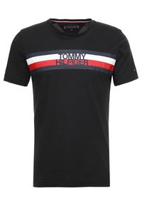 Svart bomulls t-shirt med ett horisontellt rand i vitt, rött och blått samt "TOMMY HILFIGER" tryckt i fet svart text över bröstet.