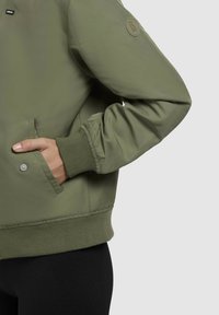 Groene bomberjack met ribbelmanchetten en -zoom, voorzien van een zijzak en een gestructureerde patch op de mouw. Soepele, lichte stof.