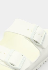 White Birkenstock sandal featuring textured straps with two adjustable buckles, a contoured footbed, and a lightweight EVA sole.