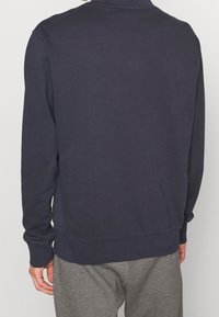 Marinblå sweatshirt med ribbad krage, långa ärmar och elastiska muddar. Har sidofållar och en avslappnad passform. Mjuk tygtextur.