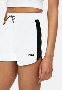 Pantaloni corti bianchi con una striscia laterale nera, realizzati in materiale leggero. Presentano una vita elasticizzata con cordino e un logo ricamato.