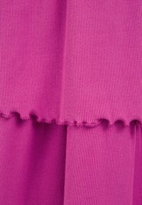 Fitted ribbat tyg i livlig rosa med en scalloped nederkant. Mjuk textur med strukturerade vertikala linjer genom hela tyget.