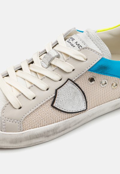 Sneakersy z beżową skórzaną i siatkową cholewką, niebieskimi akcentami i srebrnym emblematem. Oferują płaskie sznurówki oraz teksturowaną, wyglądającą na zużytą podeszwę.