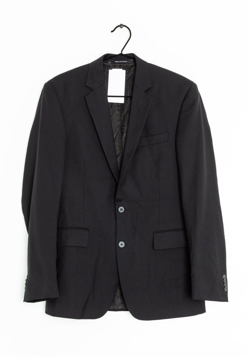 Veste de costume noire en tissu avec une texture lisse. Comprend deux poches avant, deux boutons et une poche poitrine unique. Accrochée à un crochet.