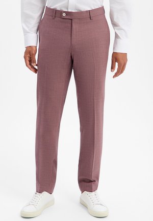 Mann trägt slim-fit staubrosa Anzughose mit Gürtelschlaufen, kombiniert mit weißen Sneakern und einem weißen Hemd.