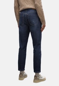 Jeans de mezclilla azul oscuro con corte slim, diseño de cinco bolsillos y un ligero desgaste. Combinados con un suéter de punto beige y zapatillas claras.