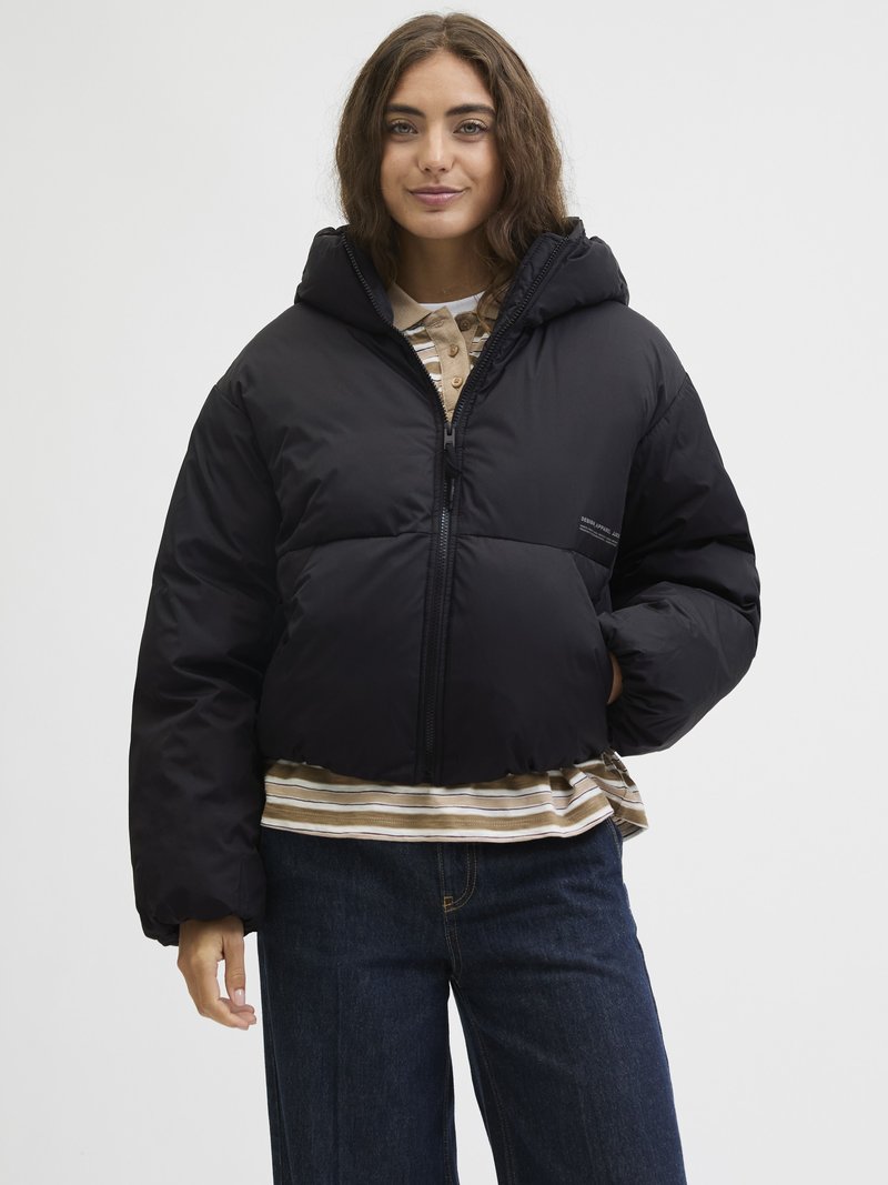 Črna puhovka z kapuco, z zadrgo spredaj in robustnim dizajnom. Model nosi črtasto majico in jeans hlače pod njo.