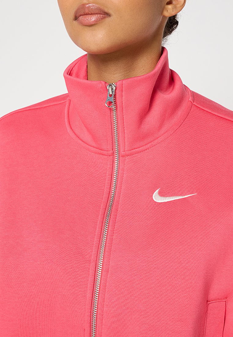 Różowy polar na zamek wykonany z miękkiego materiału, z wysokim kołnierzem, srebrnym zamkiem błyskawicznym oraz białym logo Nike na piersi.