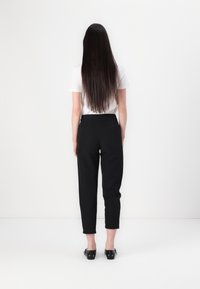 Zwarte high-waisted broek met een tapered fit, gekenmerkt door een gladde textuur en opgerolde mouwen. Gepaard met een witte top met korte mouwen.