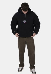 Felpa nera con zip e cappuccio, dotata di tasca frontale e logo "CRYSTAL". Abbinata a pantaloni grigi e sneakers, presenta una vestibilità comoda e il cappuccio.