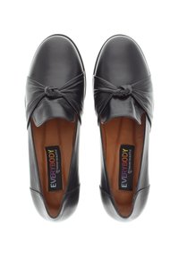 Chaussures noires en cuir à enfiler avec un détail noué au bout, texture lisse, semelle intérieure rembourrée et intérieur beige. Étiquette de marque visible.