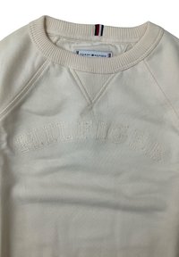 Felpa color crema con colletto a coste, caratterizzata dalla scritta "HILFIGER" ricamata in un motivo leggermente in rilievo. Texture liscia e morbida.