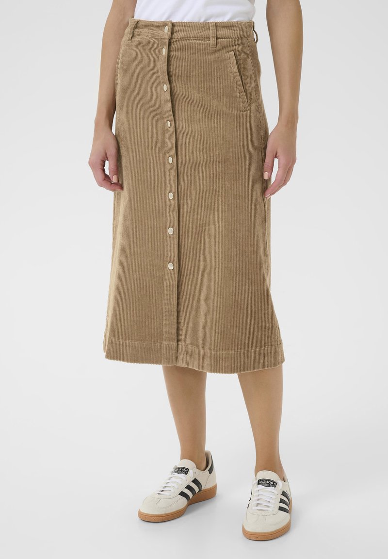 Corduroy skirt in light brown, knee-length, featuring a front button closure, side pockets, and a straight cut. Paired with white sneakers.