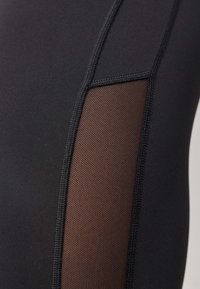 Legging de sport noir avec panneaux en maille. Tissu lisse avec des détails de couture visibles. Comprend une texture respirante en brun contrasté.