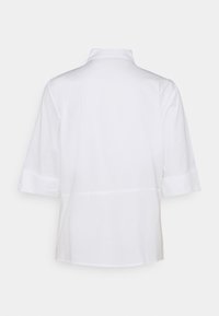 Camicia bianca a maniche corte con colletto, struttura liscia e vestibilità ampia con risvolti, progettata per un aspetto pulito e minimalista.
