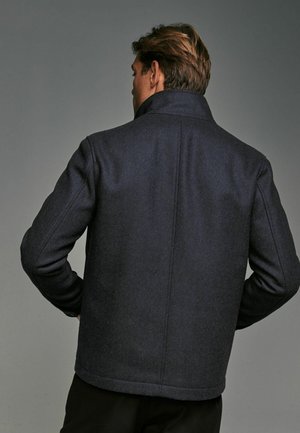 Abrigo de lana en espiga azul marino con cuello alto, corte recto y ajuste entallado. Textura suave y patrón sutil en la tela.