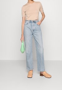 Camiseta ajustada beige, jeans de pierna ancha de talle alto en azul claro, zuecos tejidos color beige, sosteniendo un bolso verde menta. Un conjunto simple y casual.