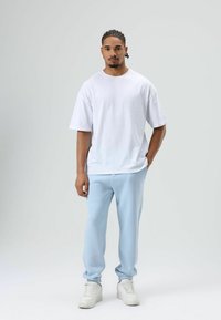 Wit oversized T-shirt, lichtblauwe joggerbroek en witte sneakers. Eenvoudig ontwerp, zachte texturen en losse pasvorm. Geen zichtbare patronen.