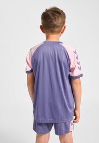 Lila sporttröja med vertikala ränder, rosa ärmar och kontrasterande detaljer. Tillverkad i ett andningsbart tyg med rund halsringning.