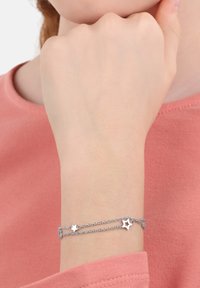 Zilveren armband met twee kettingstrengen, voorzien van stervormige bedels en een kreeftensluiting. Draagt om een pols, tegen een roze top.