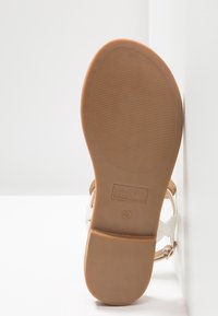 Semelle extérieure beige d'une sandale avec une surface antidérapante texturée, présentant une lanière supérieure blanche. Marquée "ANNA FIELD" et taille "37".