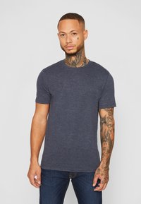 Marineblaue Kurzarm-T-Shirt aus Baumwollmischgewebe, mit Rundhalsausschnitt und einer leichten Textur. Getragen mit dunklen Jeans.
