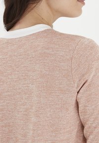 Lys rosa, tekstureret sweater med en hvid krave. Stoffet har et meleret udseende, der viser et blødt og afslappet design.