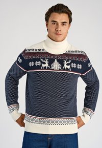 Marinblå polotröja i stickat material med krämfärgade detaljer, festliga mönster med renar och snöflingor, ribbade muddar och nederkant med kontrasterande röda ränder.