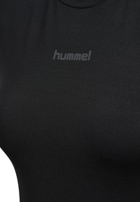 Close-up af sort stof med subtilt "hummel" logo trykt i mørkegrå, centreret nær toppen.