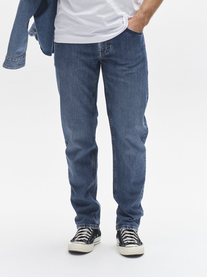 Modre kavbojke iz jeansa s krojem z ravnimi hlačnicami, zasnovo s petimi žepi in subtilnimi podrobnostmi šivov, kombinirane s črno-belimi supergami s potiskom.