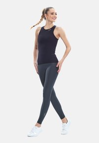Black sleeveless athletic top paired with dark grey form-fitting leggings and white athletic shoes, featuring smooth fabric and minimal design.