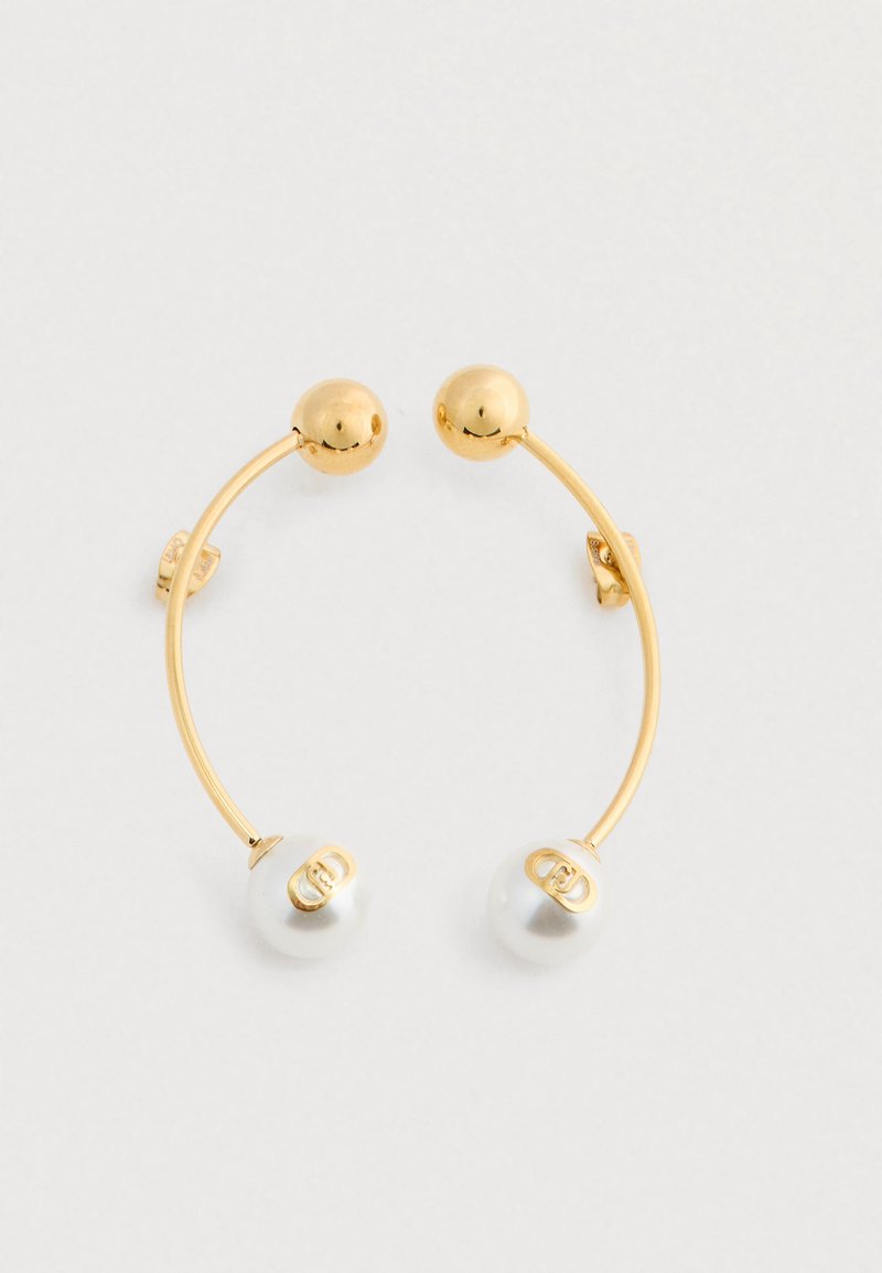 Kuldtooni kõverad lõhikud, mille ühes otsas on kuldne pall ja teises otsas valge pärl, millel on kuldne logo.