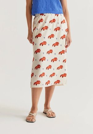 Persona que lleva una falda midi color crema con estampado de perro naranja y un pequeño corazón azul, top sin mangas azul texturizado y sandalias planas beige.