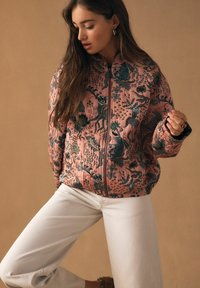 Gewatteerd jack van zachte roze stof met ingewikkelde groene bloemen- en dierenpatronen, voorzien van een rits aan de voorkant en contrasterende zwarte manchetten.