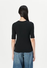 Zwarte geribbelde t-shirt met korte mouwen en een ronde hals, gecombineerd met lichtblauwe wijde jeans. Eenvoudig, getailleerd ontwerp met een gestructureerde stof.