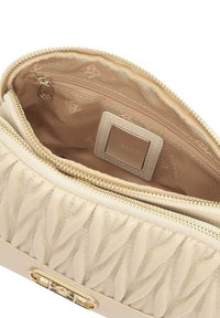 Borsa a mano in pelle beige con texture trapuntata, chiusura con zipper dorata e tasca interna con un patch logo su un rivestimento color sabbia.