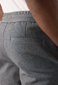 Pantaloni gri dintr-un material texturat, cu un buzunar posterior și un brâu elastic pentru confort. Vedere detaliată din lateral.