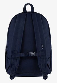 Tmavě modrý batoh s nastavitelnými polstrovanými ramenními popruhy, prsním přezkou a horním poutkem na nošení, na jednom popruhu je malý logo Polo.