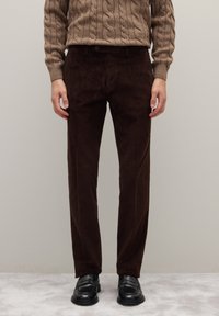 Pantalones de pana marrón con corte recto, con canaletas verticales. Combinados con mocasines negros y un suéter marrón texturizado.