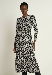 Schwarzes und cremefarbenes gemustertes Kleid mit langen Ärmeln, rundem Ausschnitt und tailliertem Oberteil, das ein geometrisches Design aufweist.