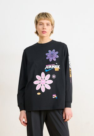 Svart langermet T-skjorte med fargerike blomstergrafikk i rosa og lilla, med logoer og tekst på fronten og på ermet. Bomullstekstur.