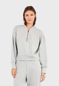 Grijze rits-sweater met hoge kraag, losse pasvorm, geribde manchetten en een cropped zoom. Glad textuur, minimale details.